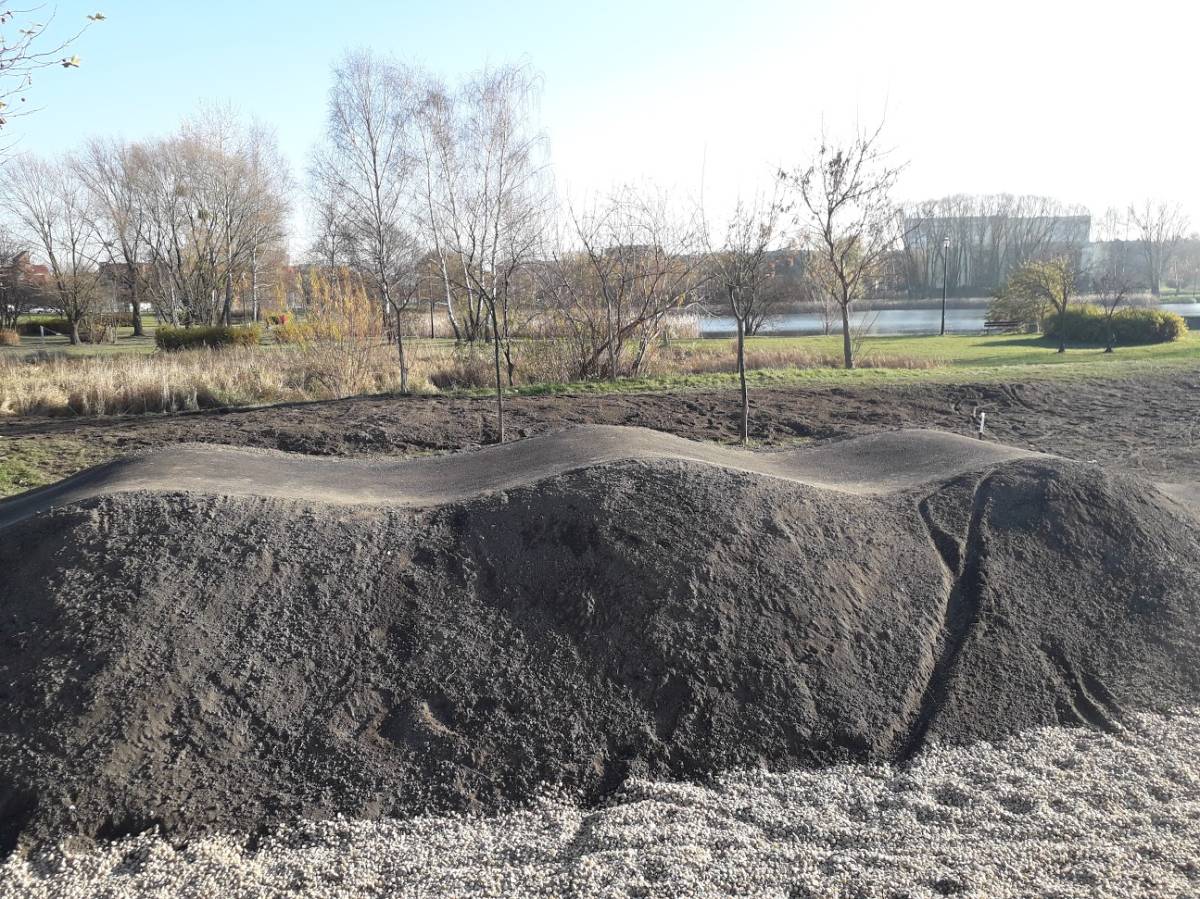na pierwszym planie pumptrack, na drugim staw 
